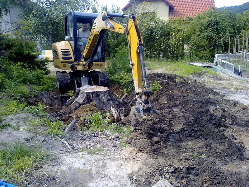 Pásový minibagr při odstraňování pařezu na zahradě u rodinného domu